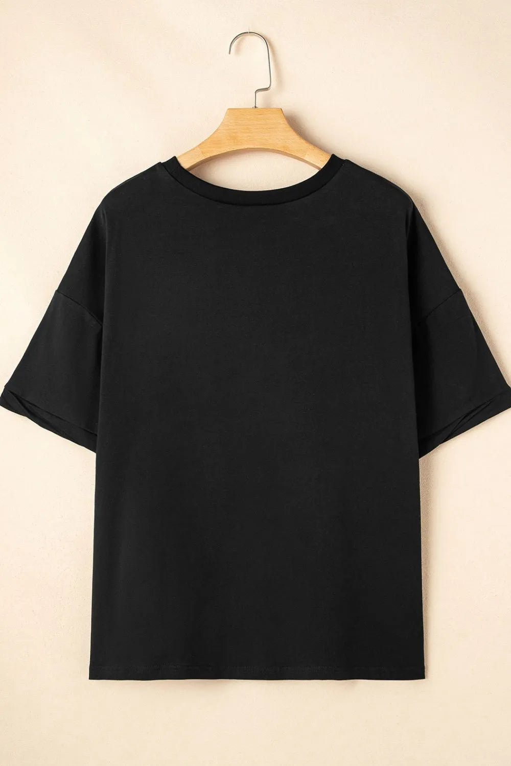 Black t-shirt on a wooden hanger against a beige background