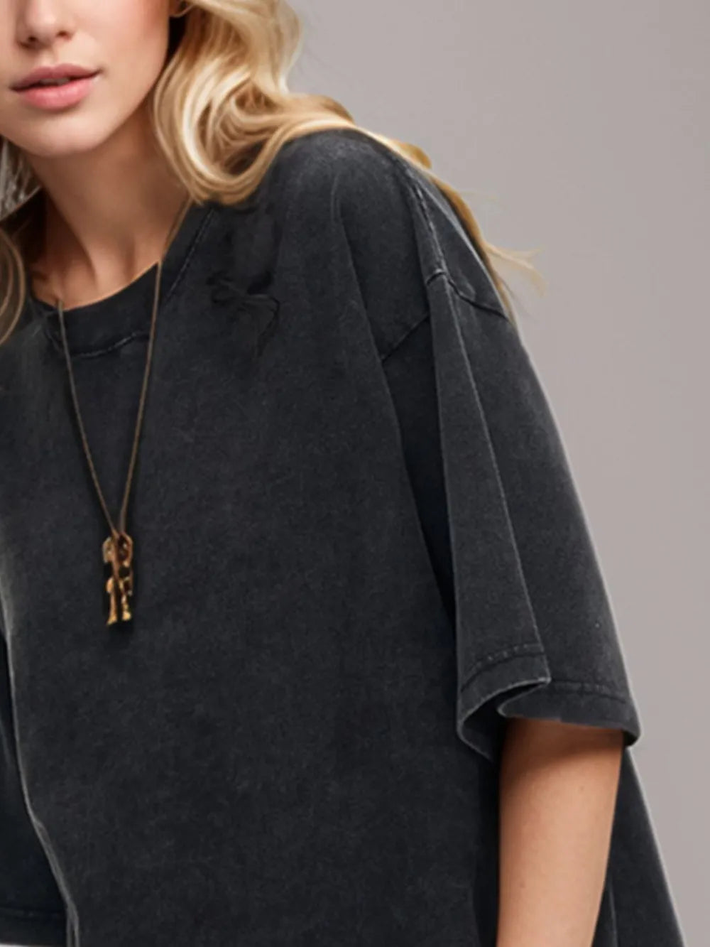 Person wearing a black oversized t-shirt with a necklace featuring two small figures on a plain background