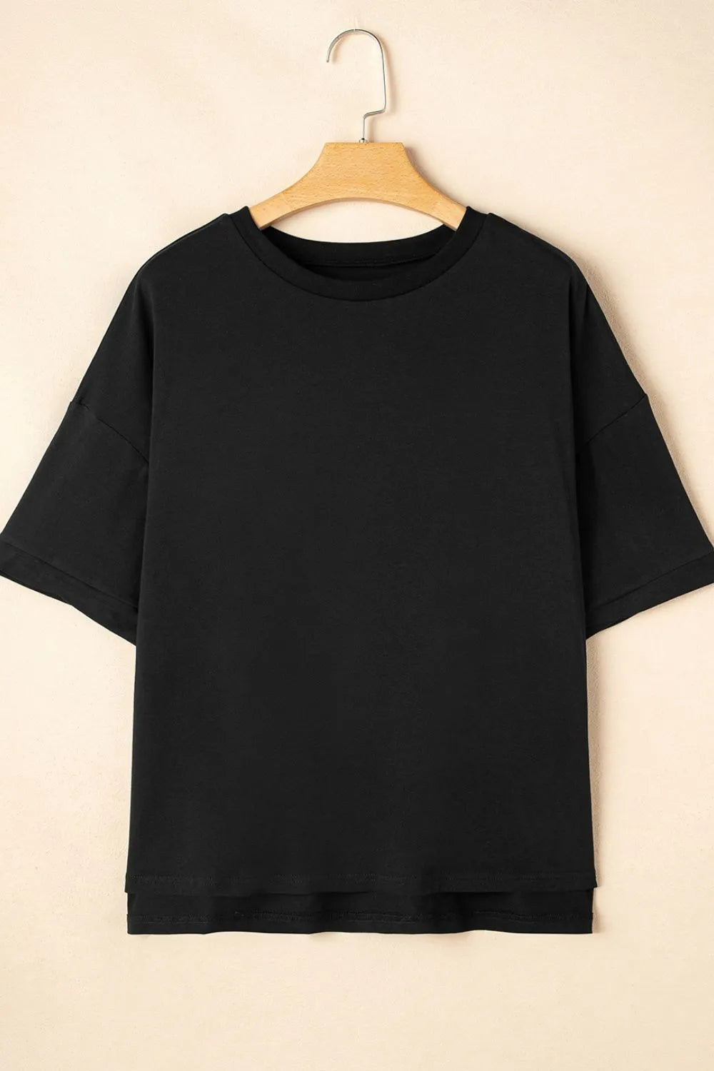 Black t-shirt on a wooden hanger against a beige background