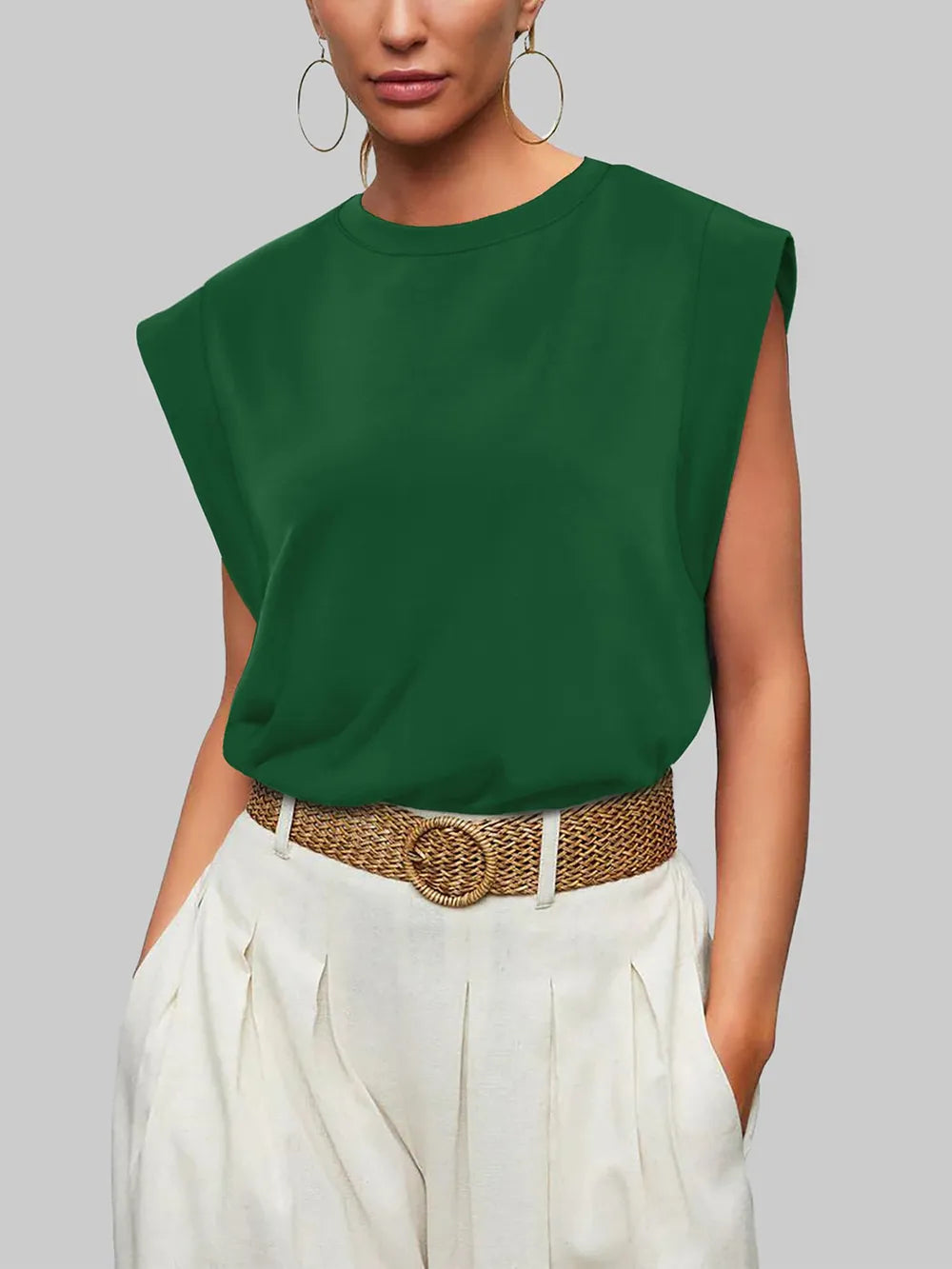 Person wearing a green sleeveless top and white pants with a brown belt against a gray background