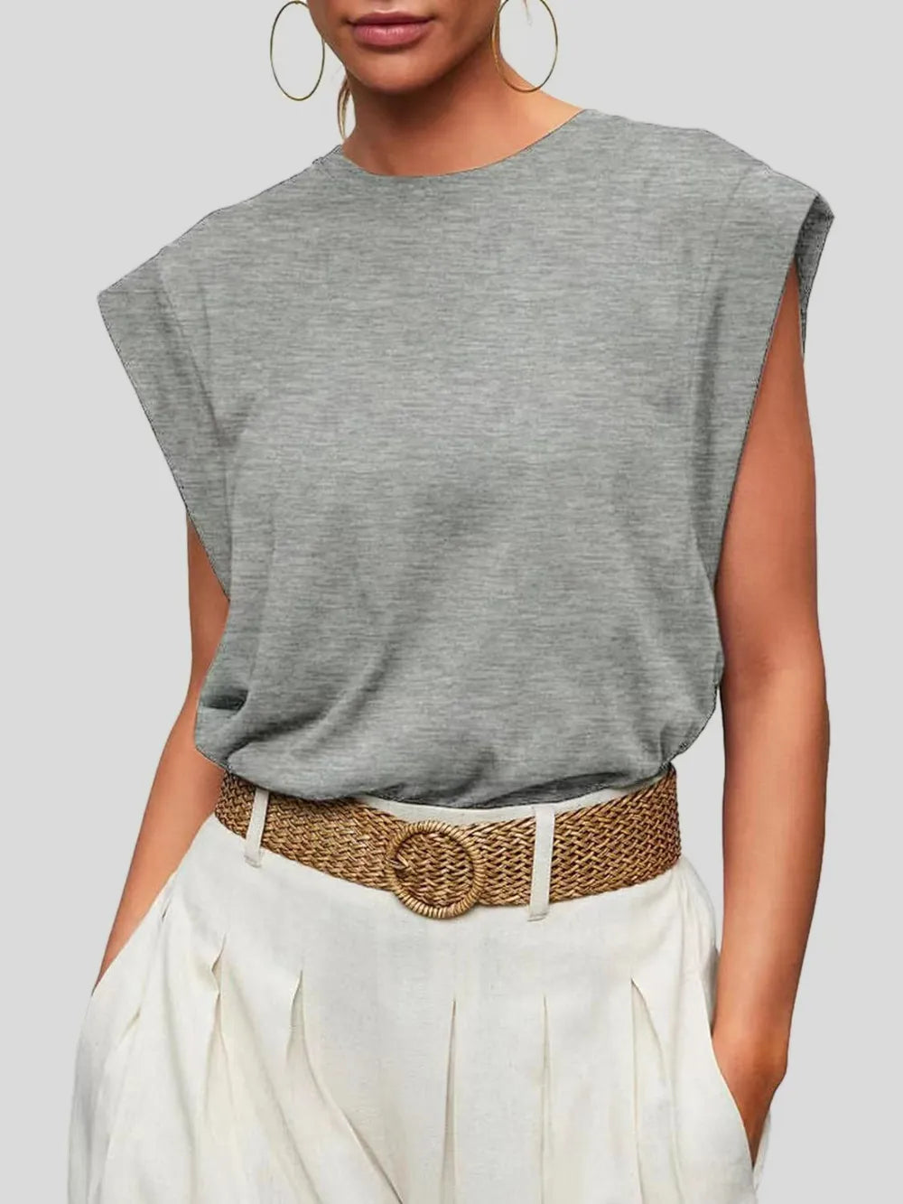 Person wearing a gray sleeveless top with a brown belt and white pants on a light gray background