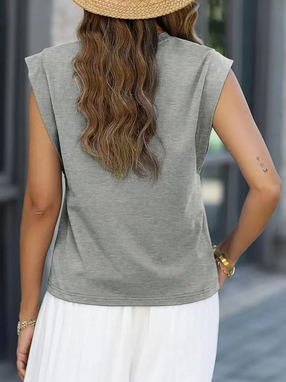 Person wearing a gray sleeveless top and white pants with a blurred background