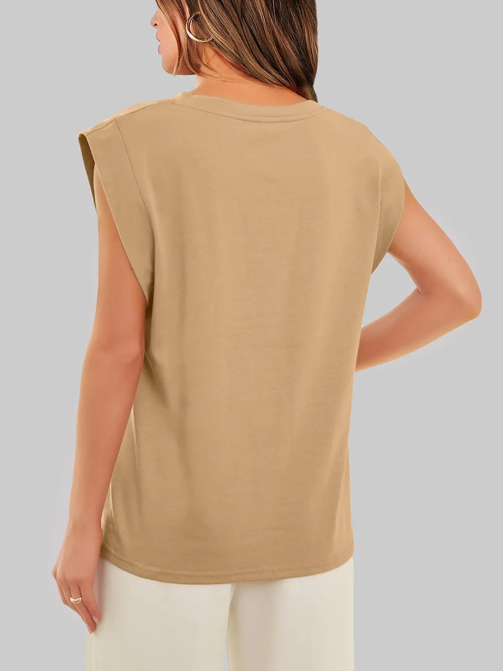 Woman wearing a beige sleeveless top against a plain background