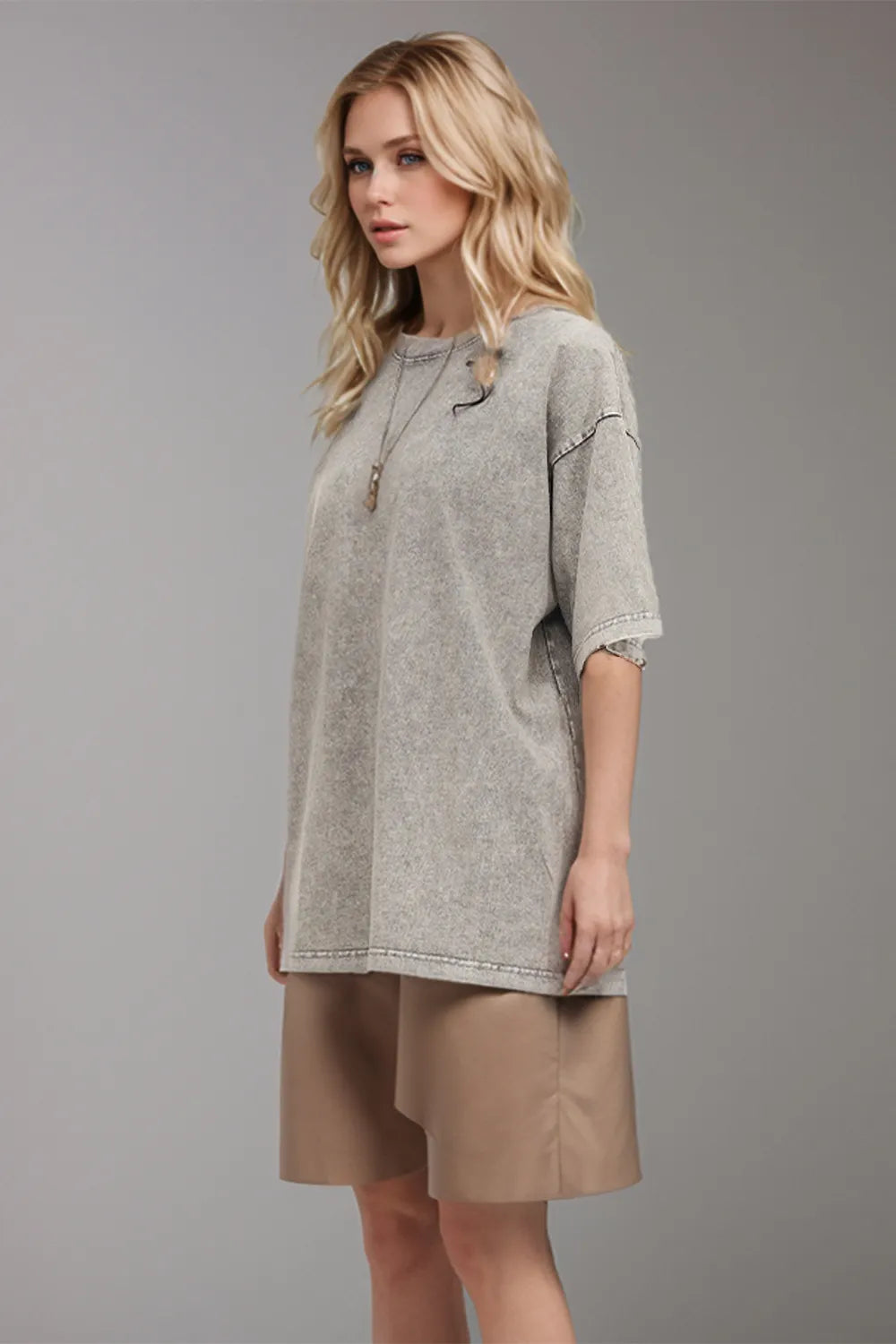 Woman wearing a gray tunic and beige skirt on a gray background