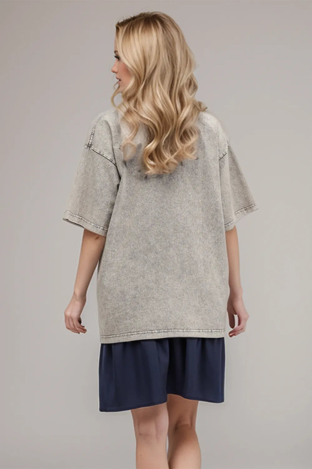 Woman wearing a gray oversized t-shirt and navy shorts on a plain background