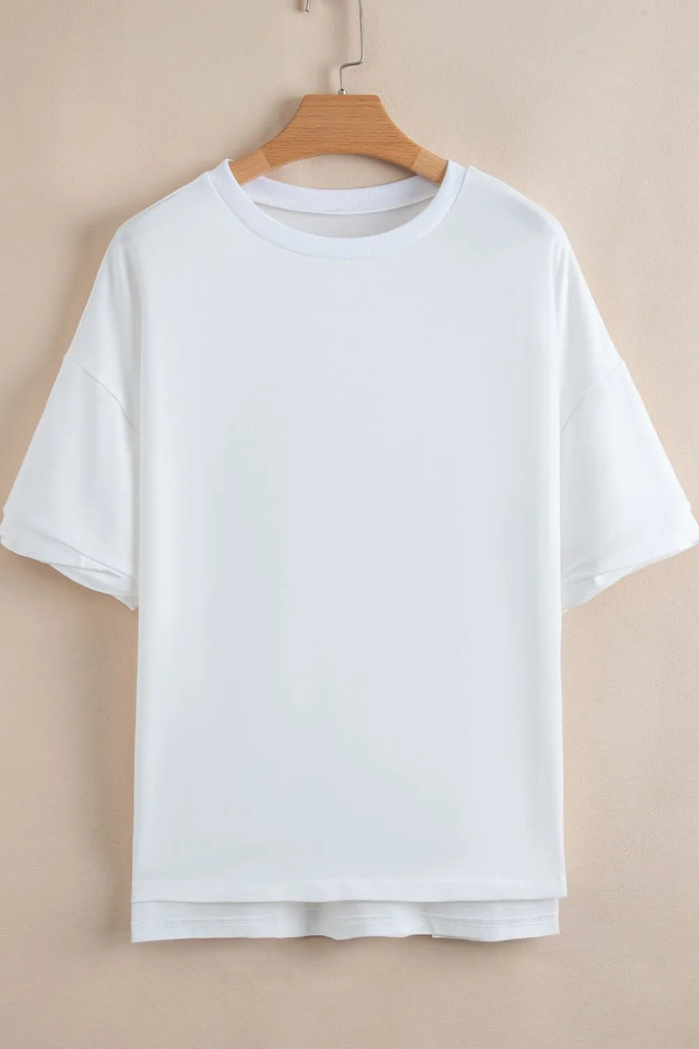 White t-shirt on a wooden hanger against a beige background