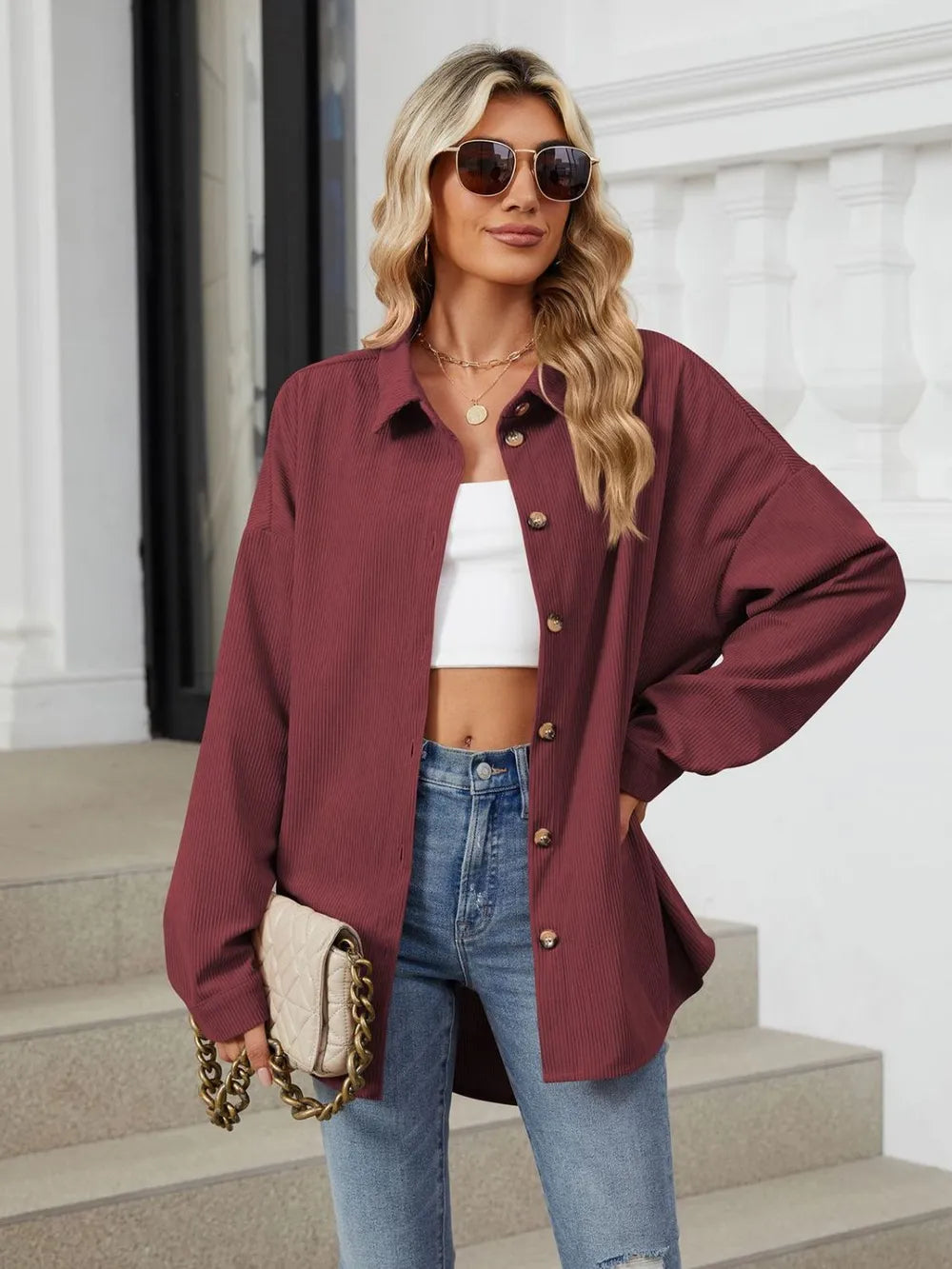 Woman wearing a burgundy jacket, white top, and blue jeans outdoors.