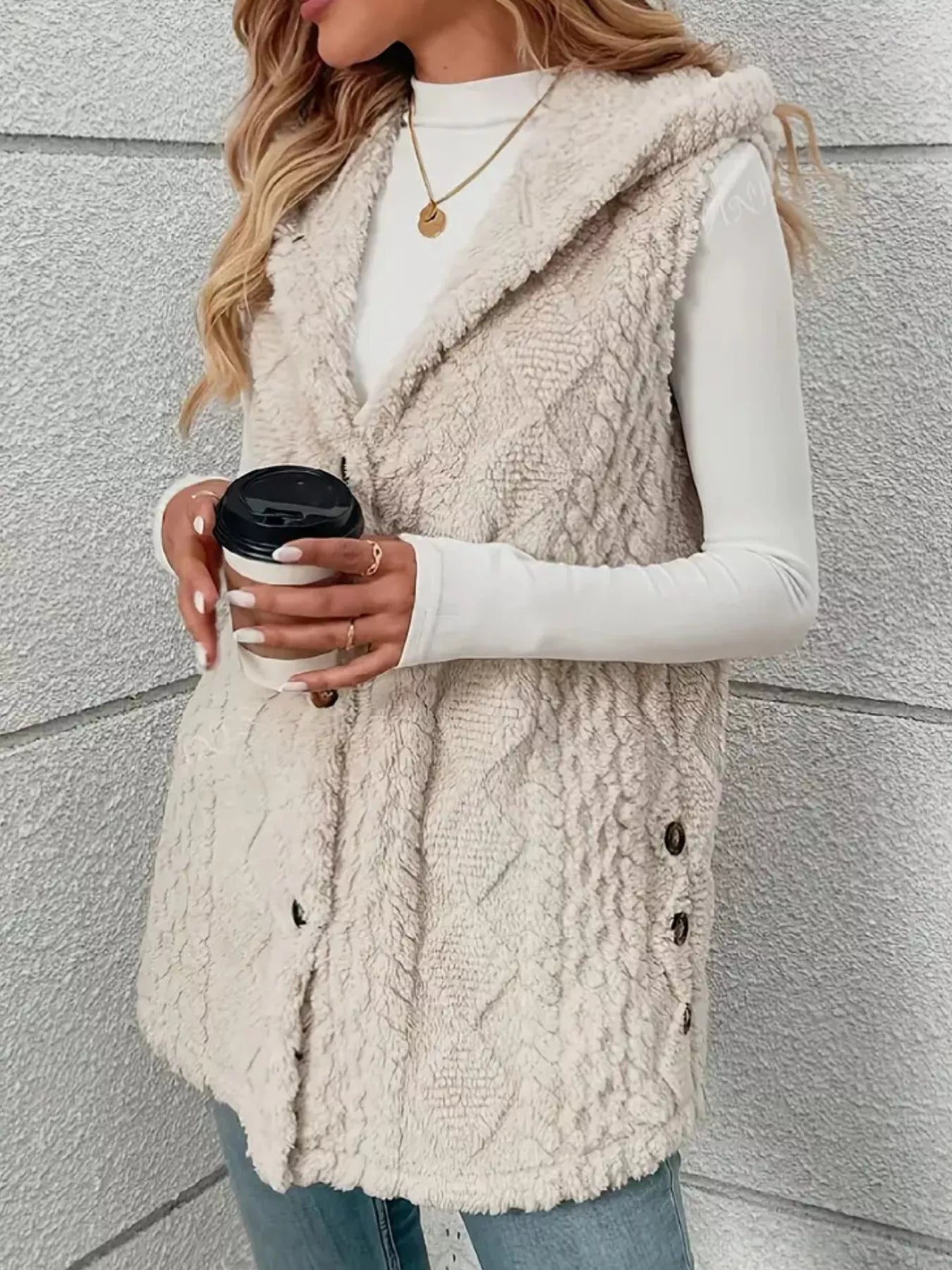 Woman layering cream hooded sherpa vest over gray sweater and jeans