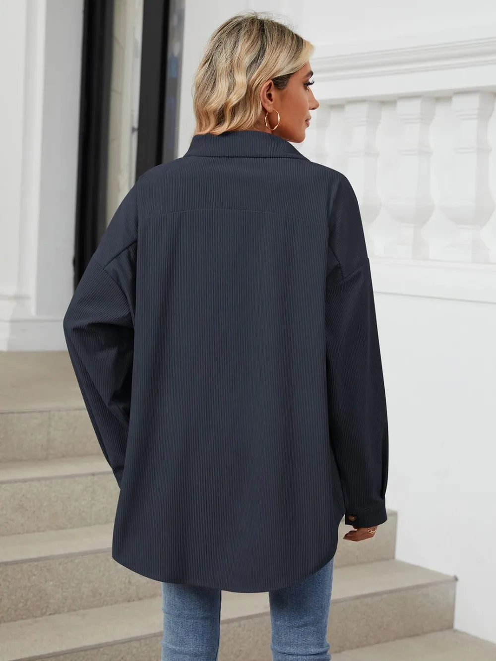 Person wearing a dark blue coat standing on steps with a white wall in the background