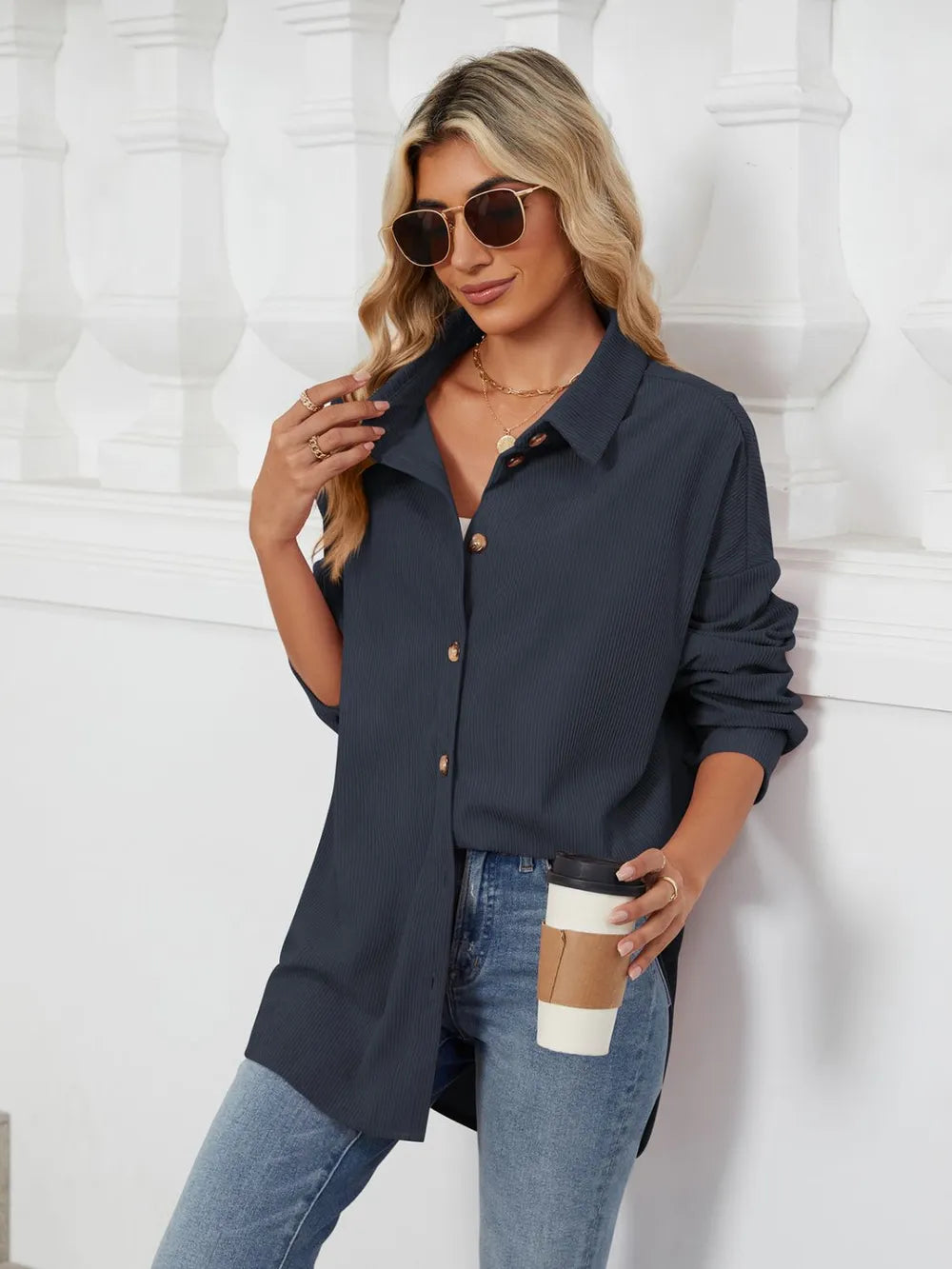 Woman wearing a navy shirt and jeans, holding a coffee cup against a white background