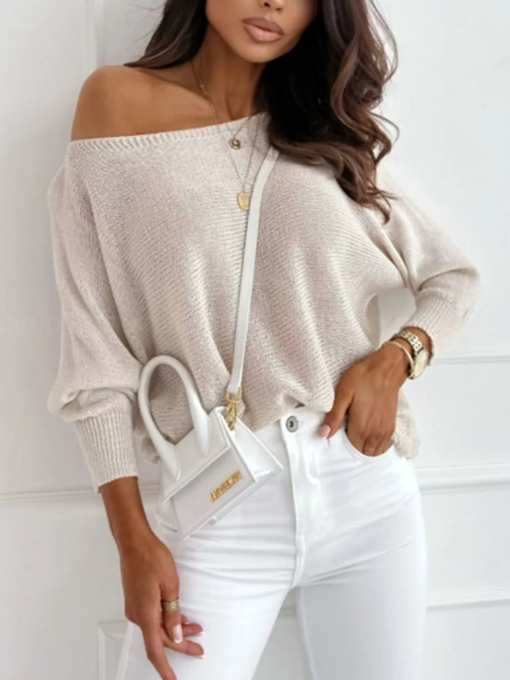 Neutral cream bow back off-shoulder sweater, perfect transitional season piece
Woman wearing a beige off-shoulder sweater and white pants, holding a white handbag.
