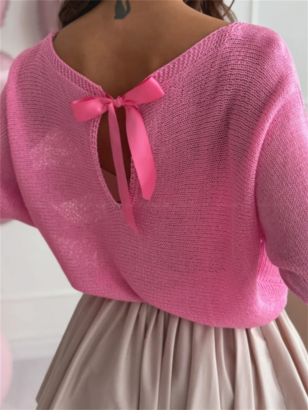 Evening styling: bow back sweater with bold earrings and sleek hair

Pink knitted top with a bow detail on a plain background