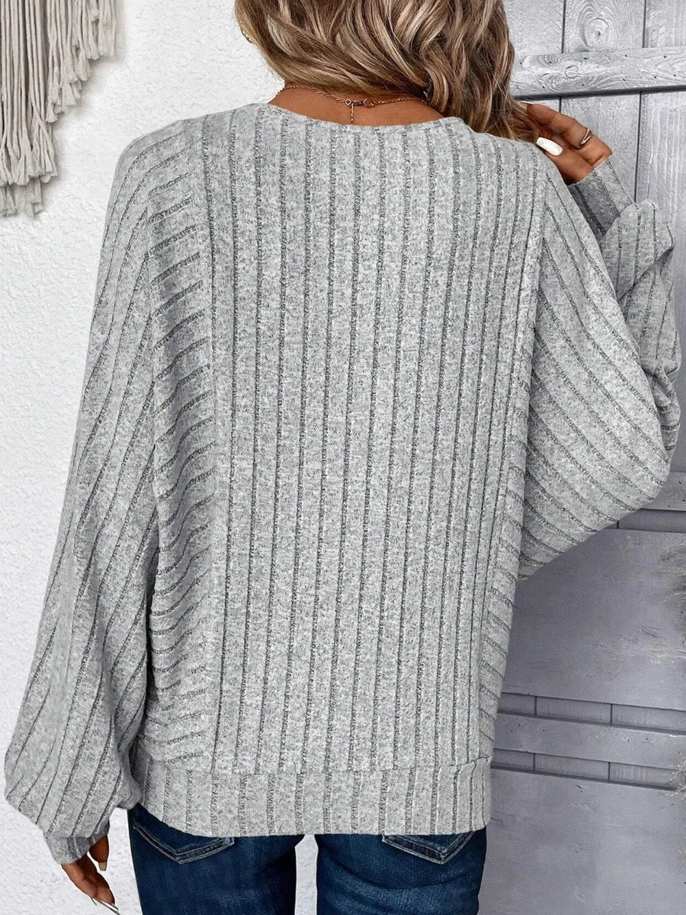 Person wearing a gray ribbed sweater with a neutral background