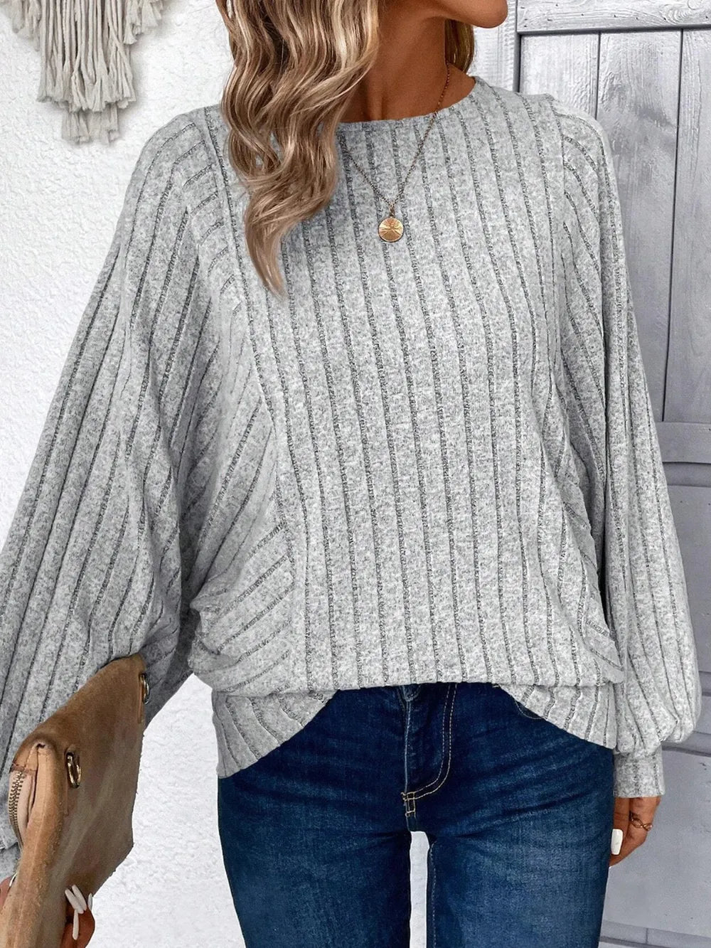 Person wearing a gray ribbed sweater and blue jeans, holding a beige purse.