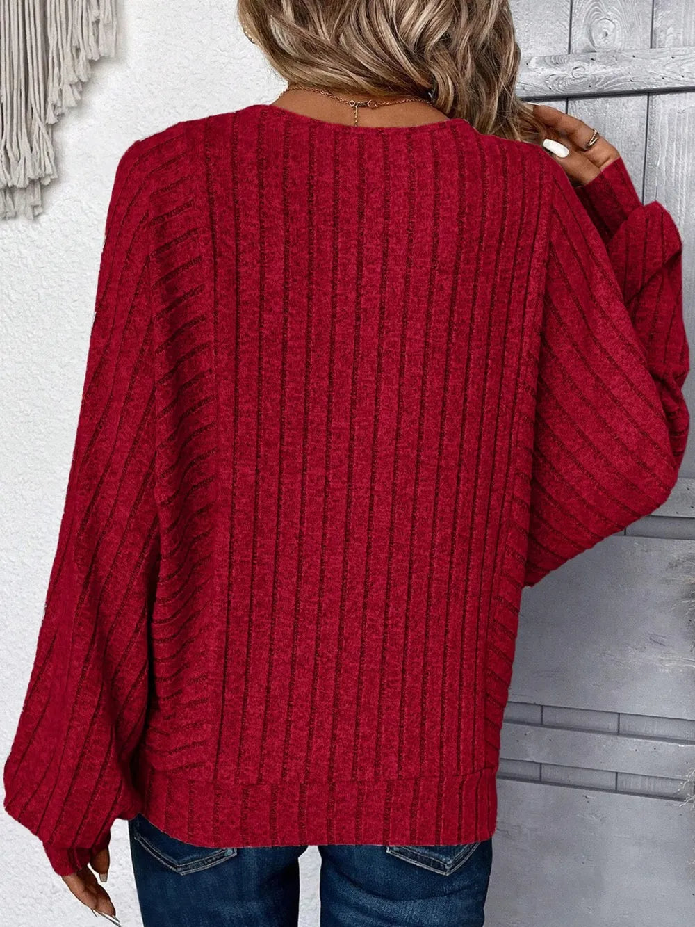 Person wearing a red ribbed sweater with a neutral background