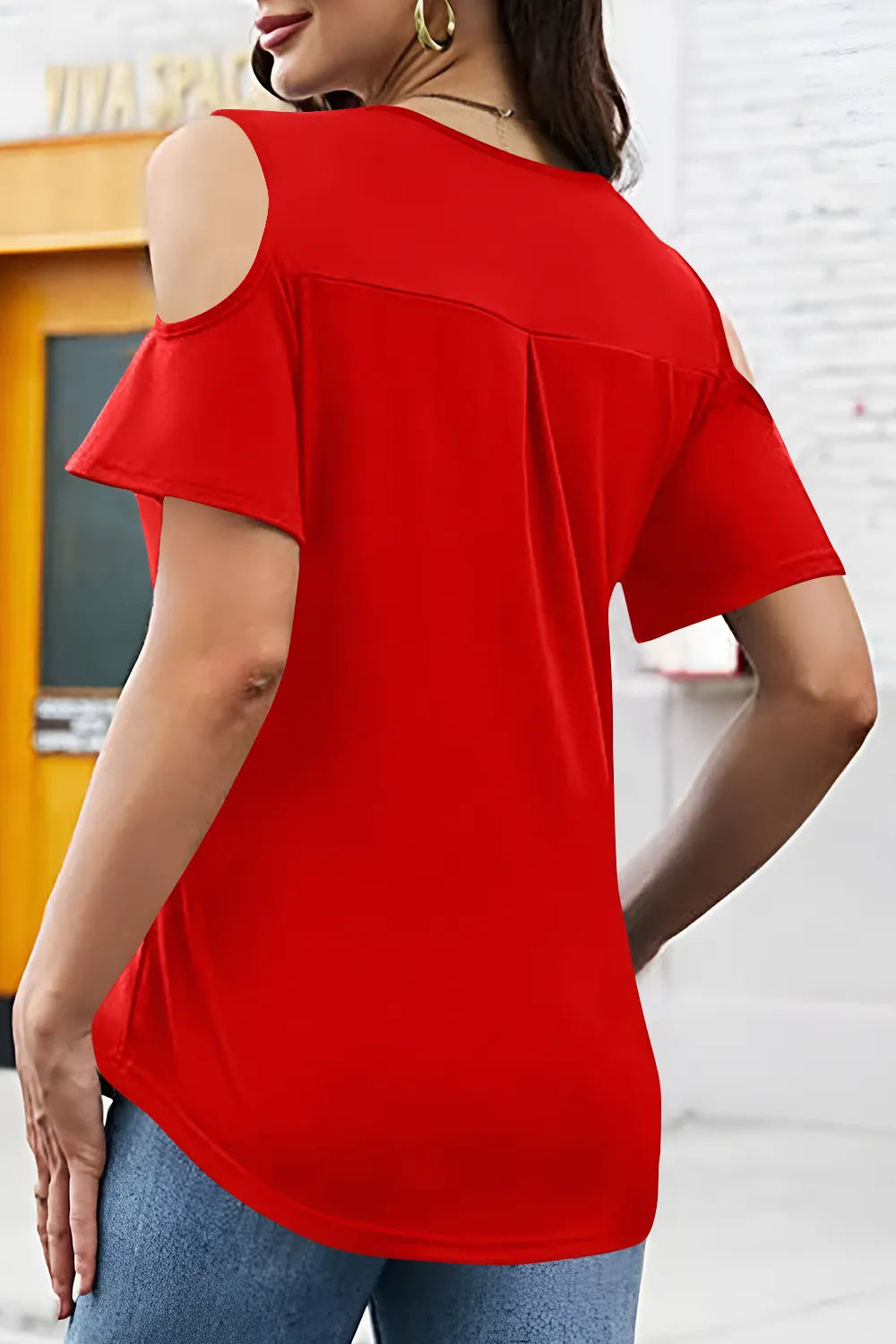 Red top with cut-out shoulder design worn by a person, with a blurred background.
